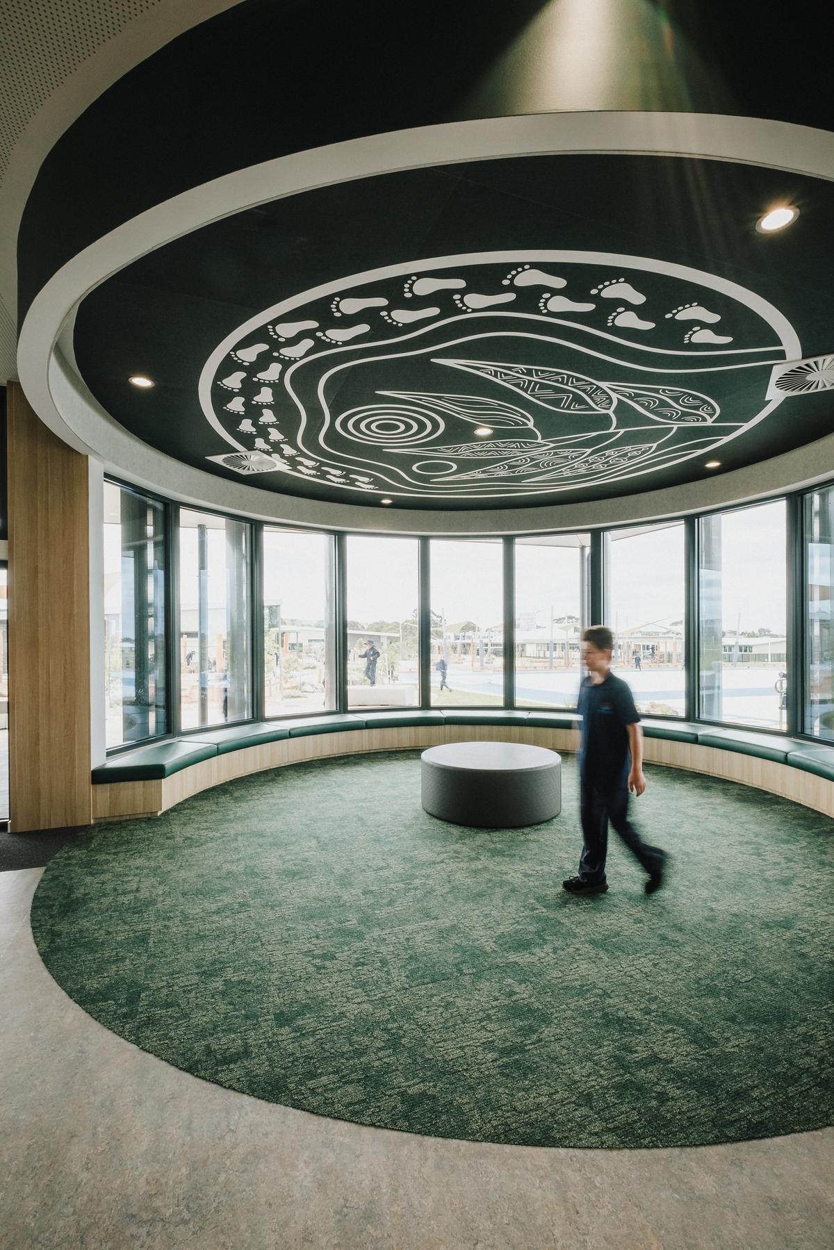 Circular indoor space with patterned ceiling feature and wraparound windows, with a student walking through