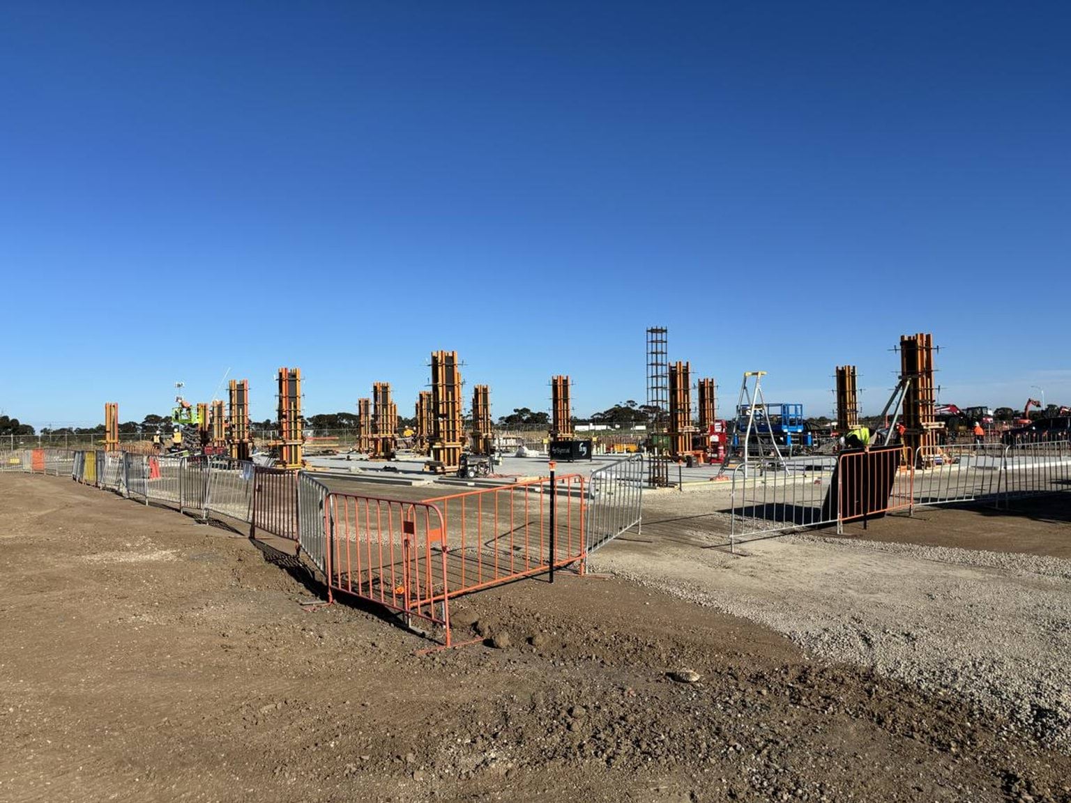 Construction site with multiple concrete column formworks and safety barriers on cleared ground