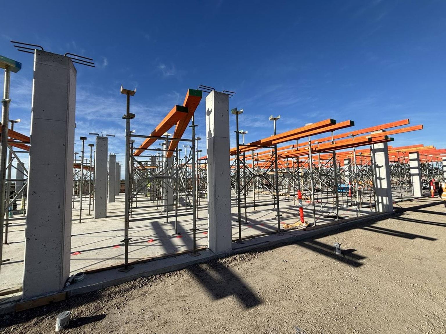 Partially built structure with concrete columns, scaffolding and orange beams under clear sky