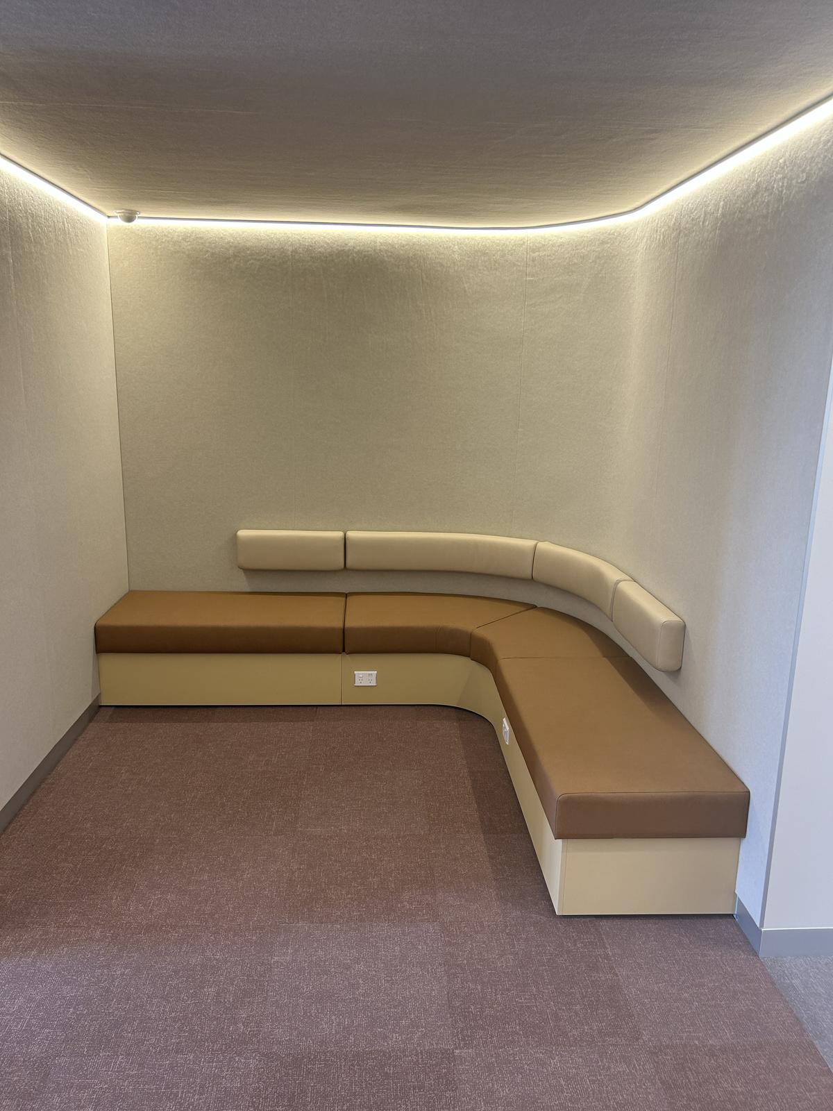 A quiet breakout space with an L-shaped cushioned bench against light-coloured walls and soft lighting along the ceiling edge.