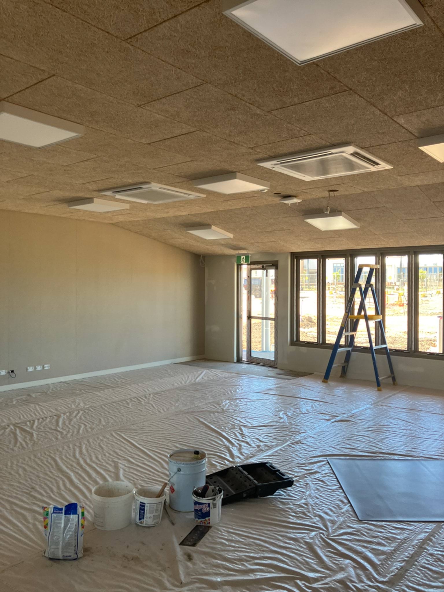 A partially completed school building with brick and metal walls, large windows, and unfinished ground surfaces.