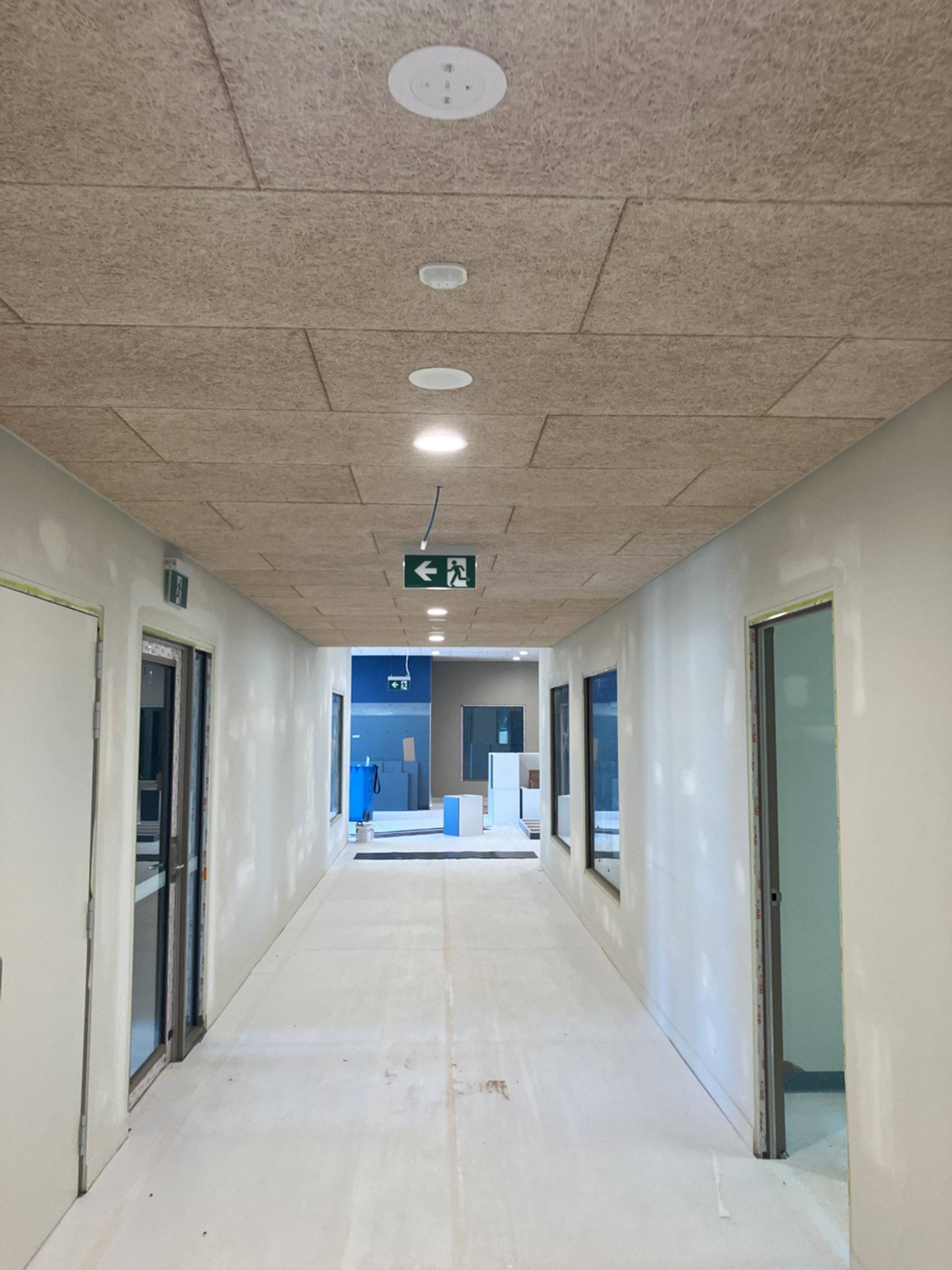A long corridor with white walls and ceiling panels installed, leading to unfinished rooms with visible wiring.