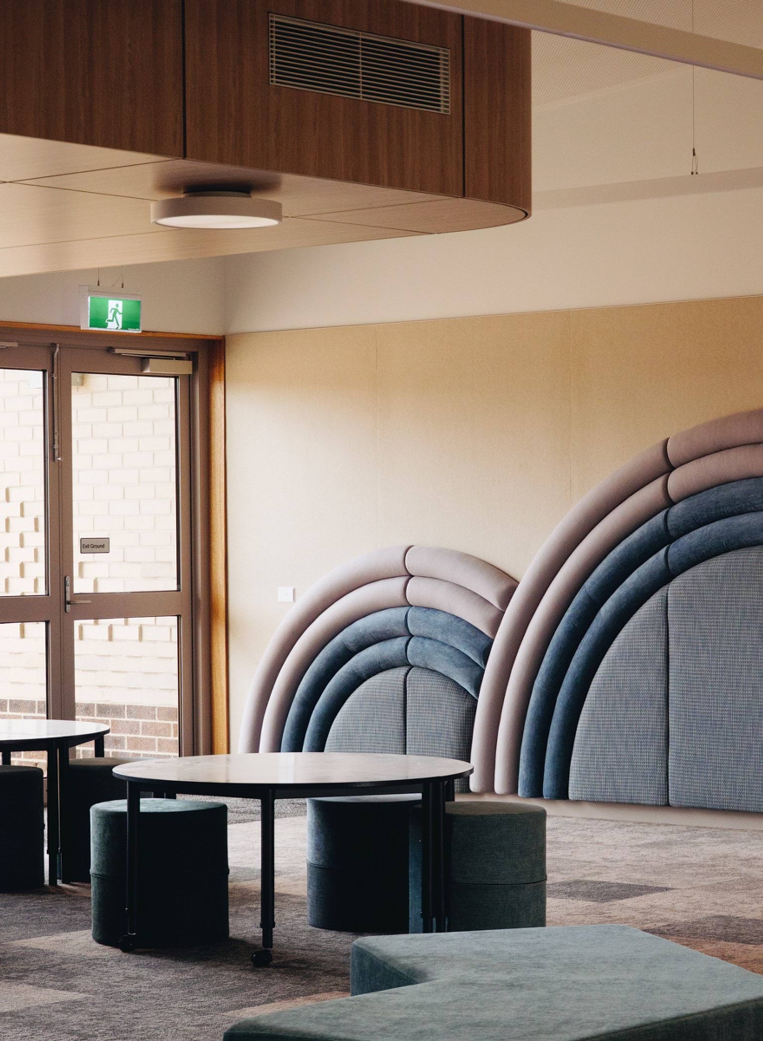 Indoor breakout space with curved upholstered wall seating, round tables and timber ceiling bulkhead