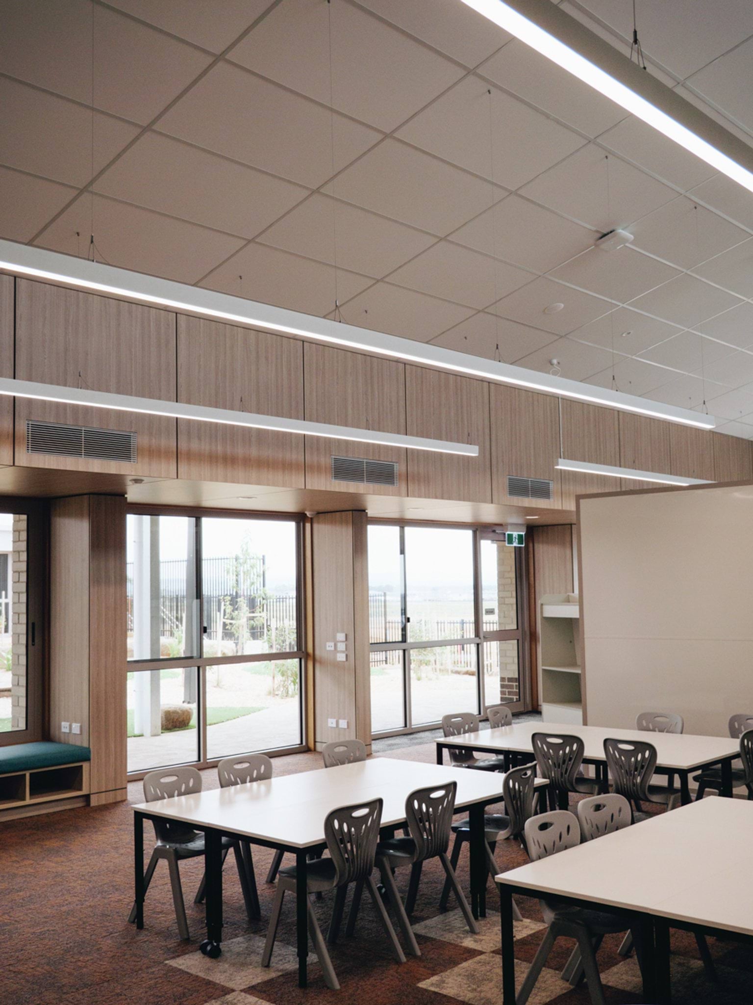 Classroom interior with grouped tables, timber wall linings, suspended lighting and large glazed doors