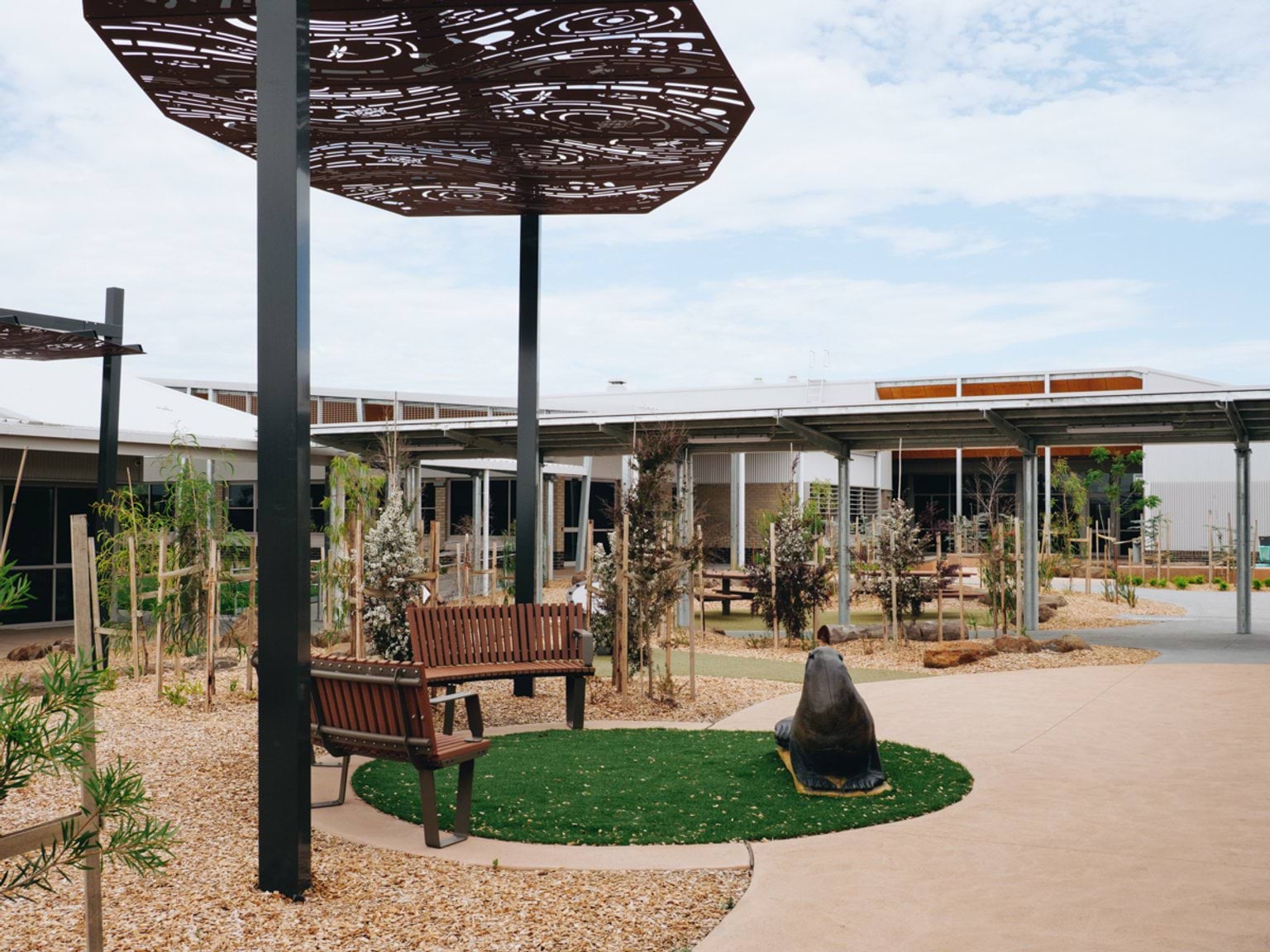 Outdoor seating area with perforated metal shade canopy, concrete paths and surrounding classroom buildings