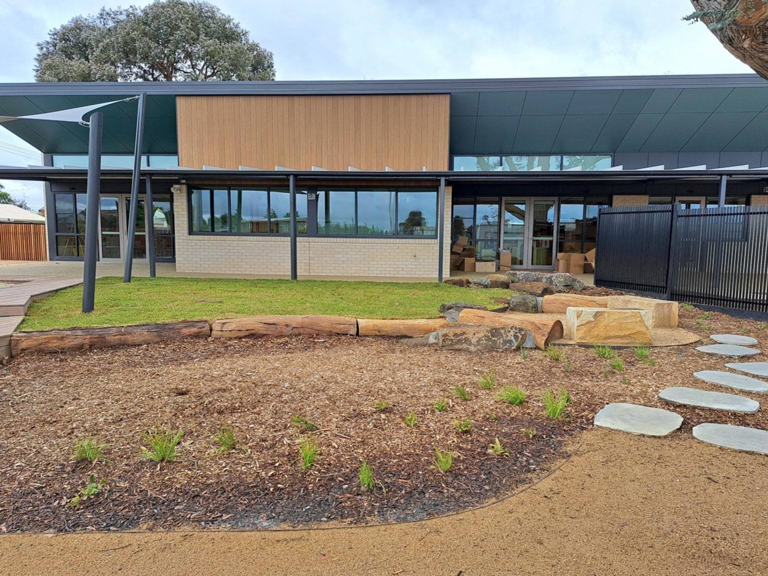 The rear of the kindergarten building with large windows, a landscaped play area, stone steps, and young plantings.