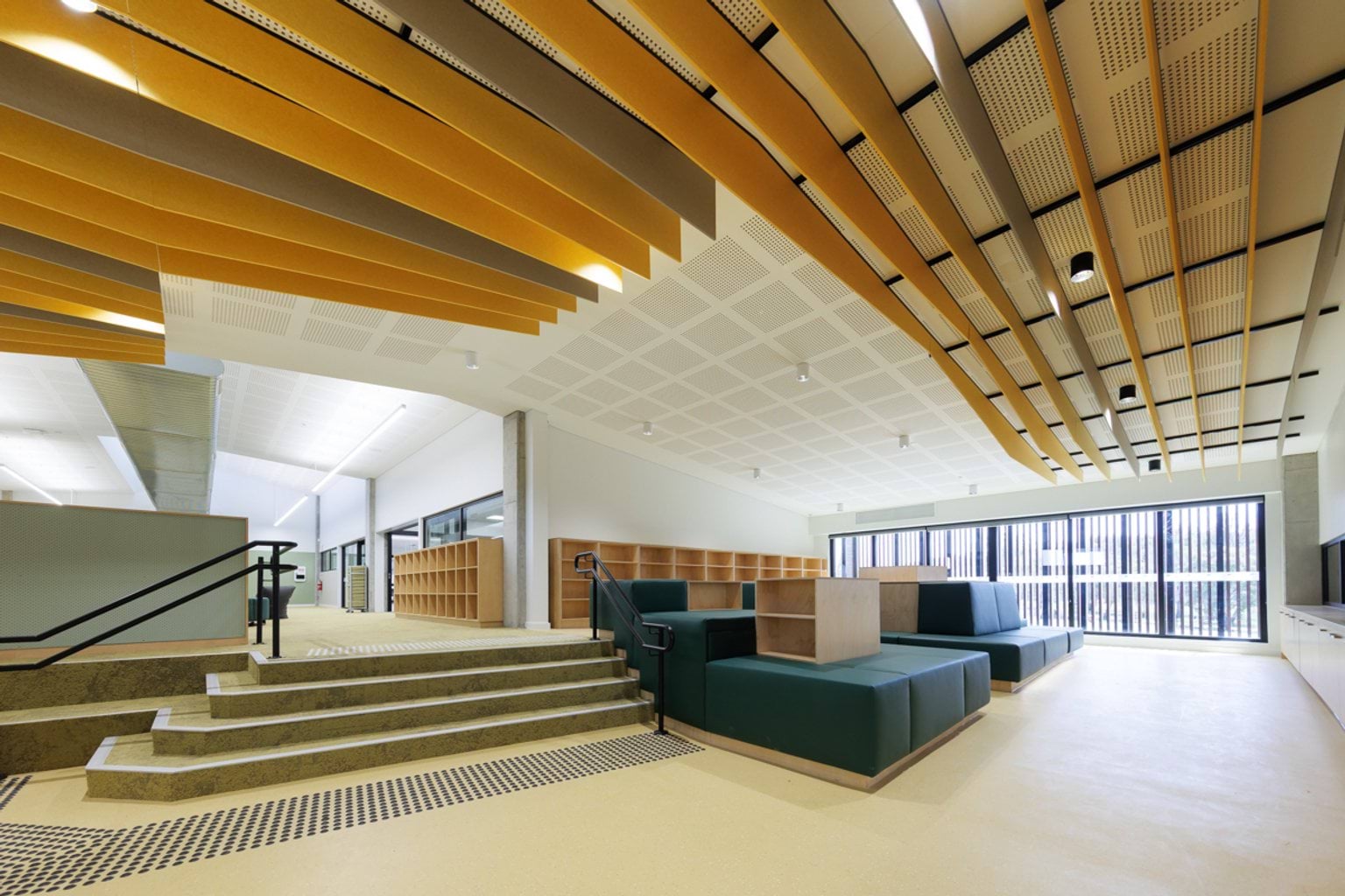 Learning space with stepped seating, timber storage benches and yellow acoustic ceiling fins.