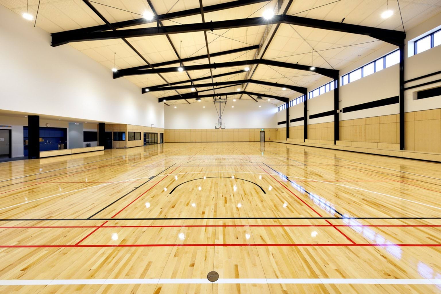 Indoor sports court with polished timber flooring, high ceilings, marked game lines and basketball hoops