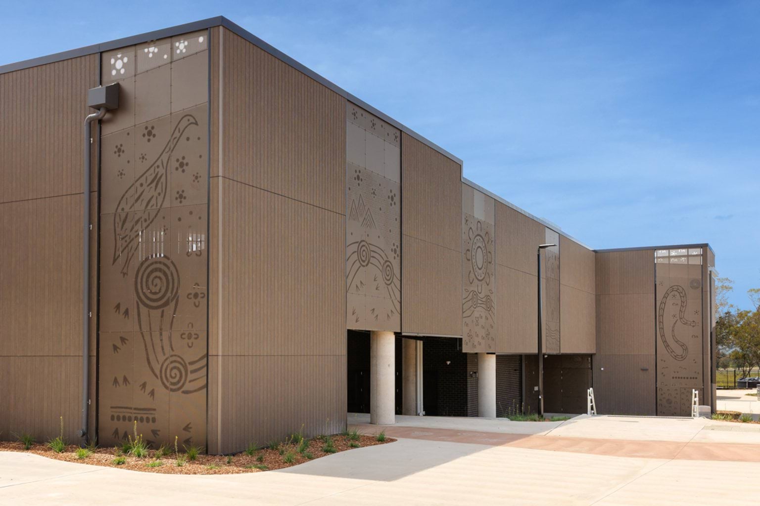 Exterior of a modern school building with vertical cladding and large decorative panels featuring Indigenous-inspired artwork.