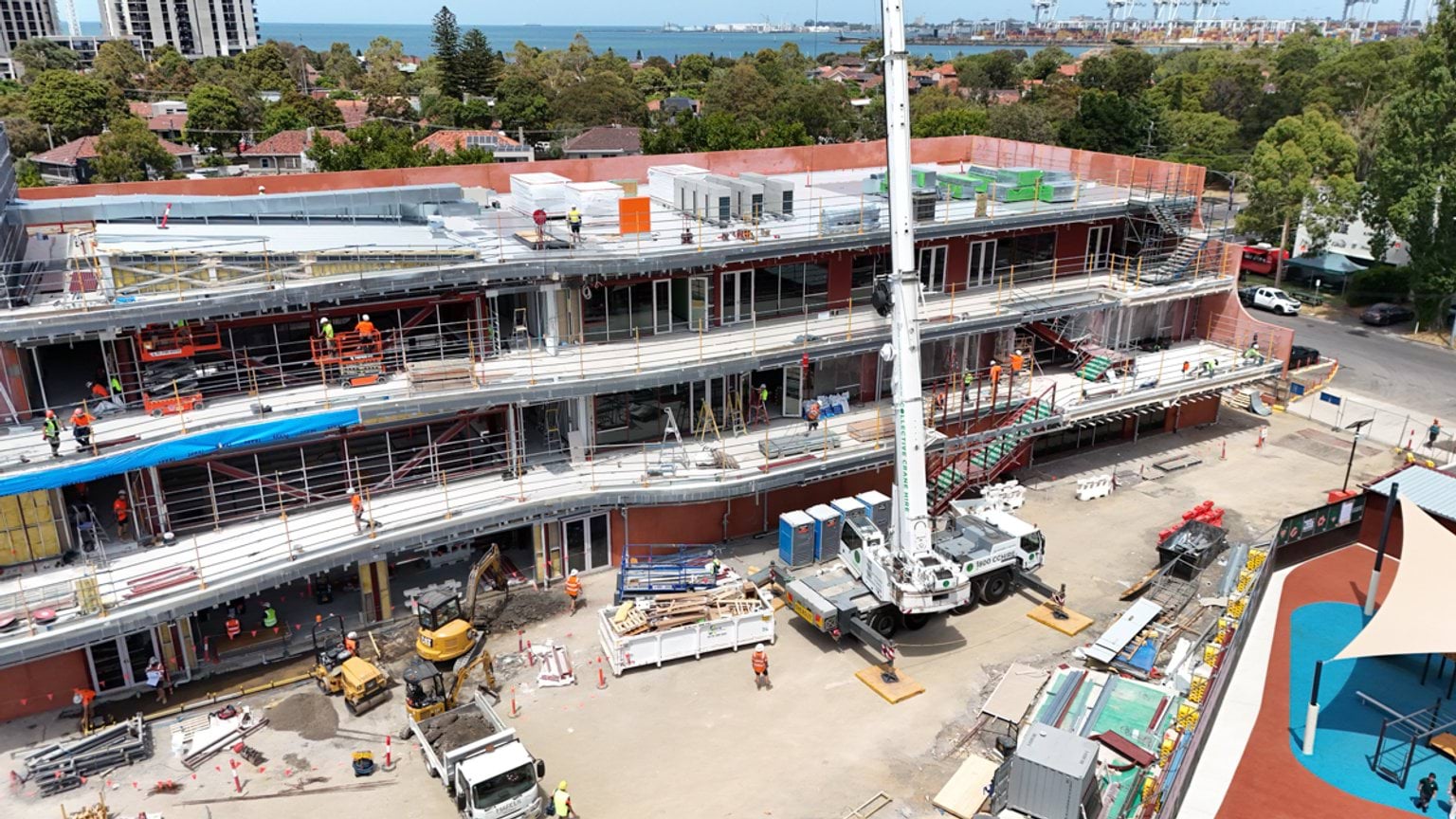 Aerial view of multi‑storey school building under construction with scaffolding, crane and workers on site