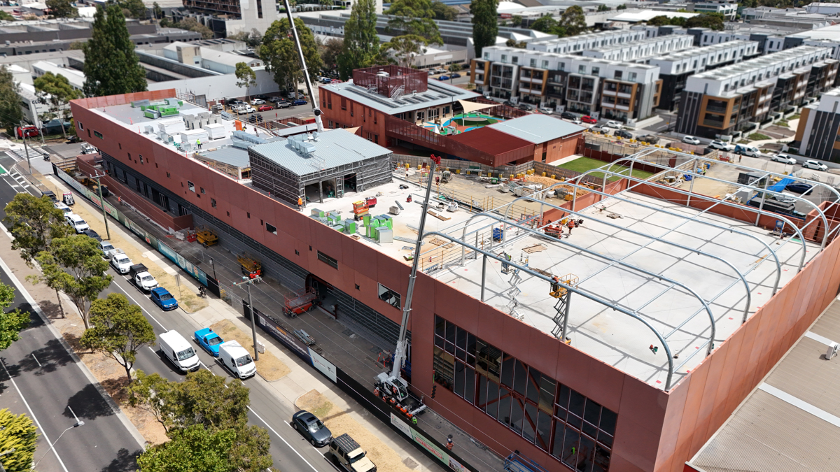 Aerial view of large construction site showing roof installation, scaffolding and surrounding residential area