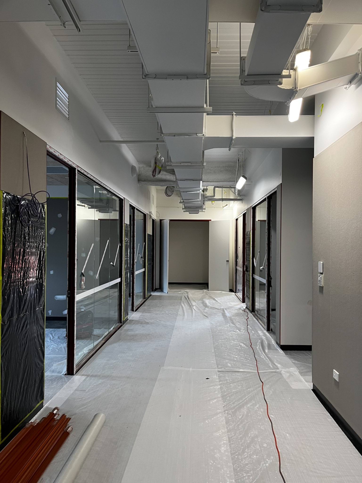 Internal corridor under construction with exposed ductwork, unfinished glazing and protective floor sheeting