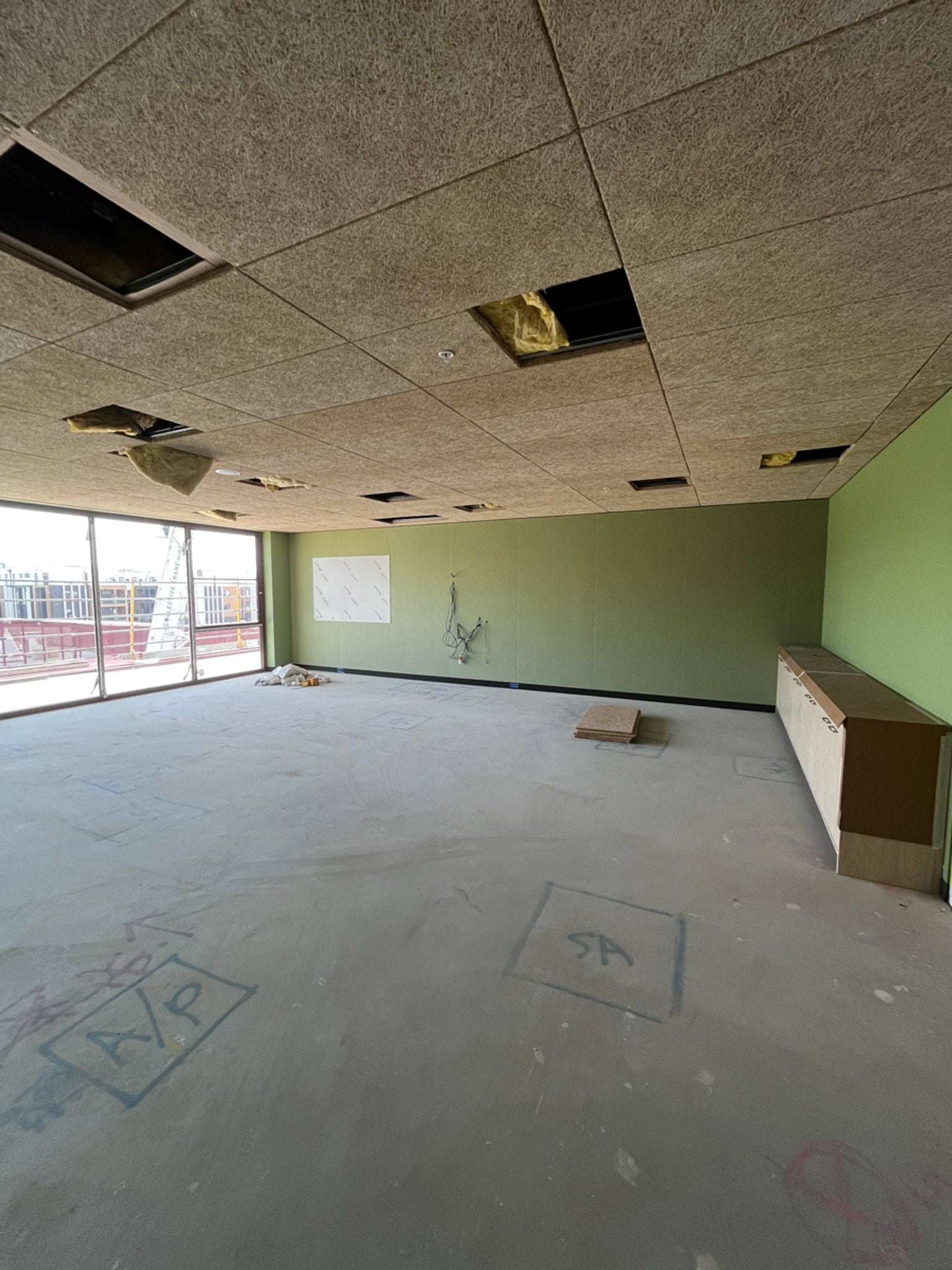 Classroom space with green feature wall, unfinished ceiling panels and concrete floor marked for services