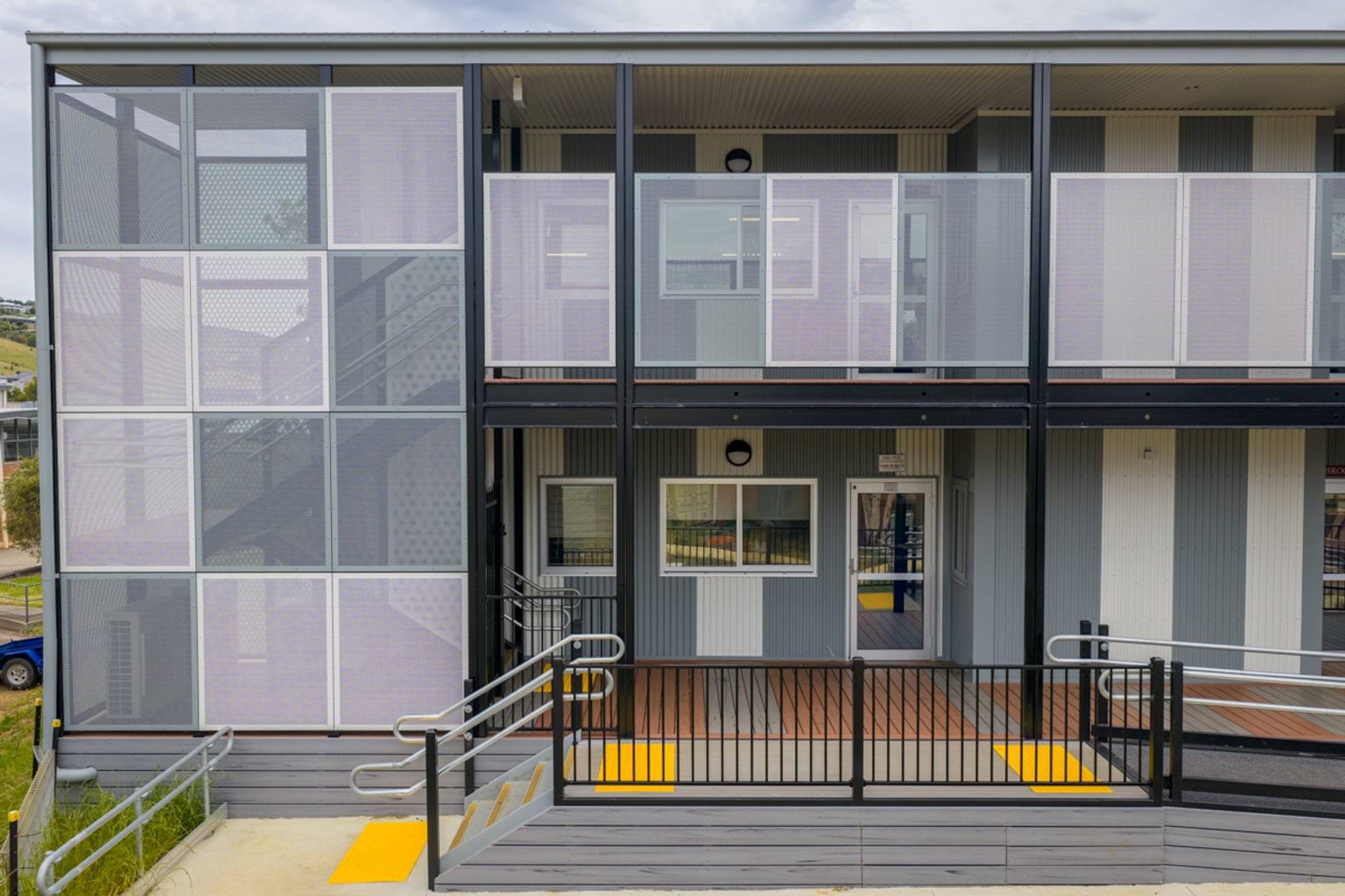 The exterior of a two‑storey modular school building with screened balconies, ramps, and contrasting grey wall panels.