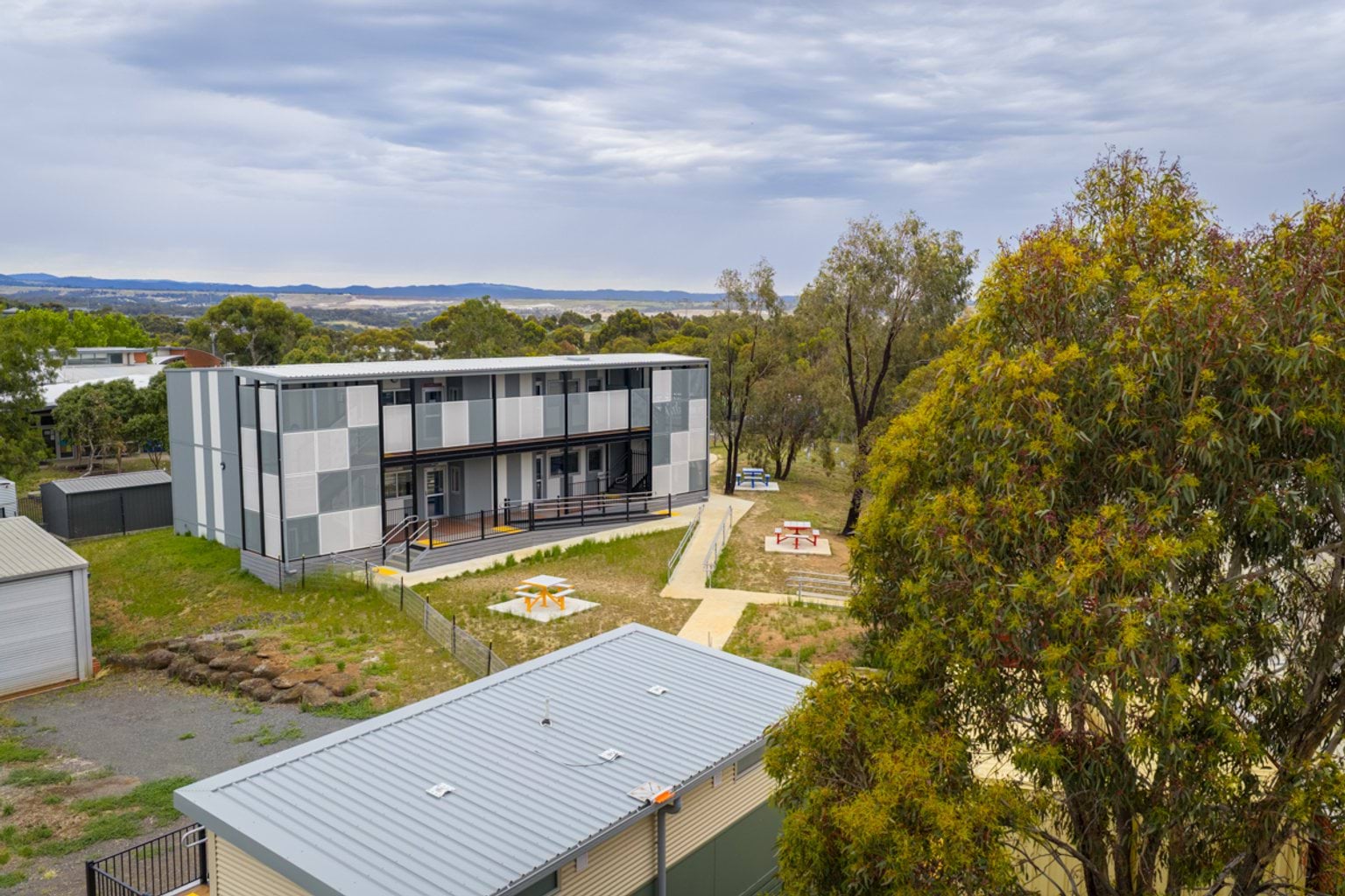 An elevated view of the modular school building set among trees, with pathways and outdoor seating areas nearby.
