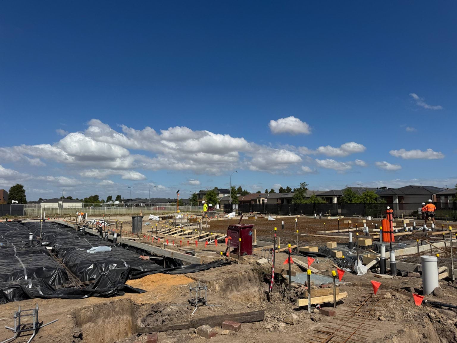 School construction site with services installation underway, including piping and marked foundations.