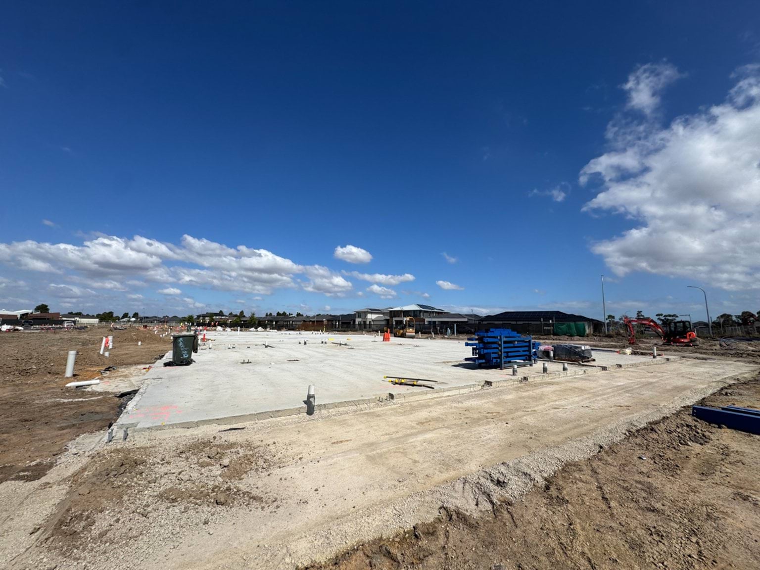 A wide concrete slab newly poured on a school construction site, with tools and materials stacked nearby.
