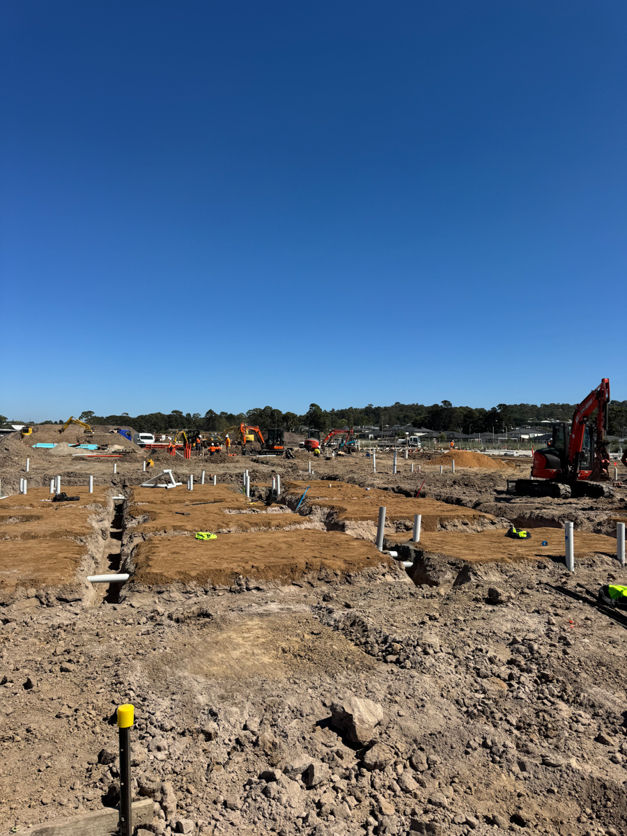 Trenches and pipework being installed across a large construction site, with excavators operating in the background.