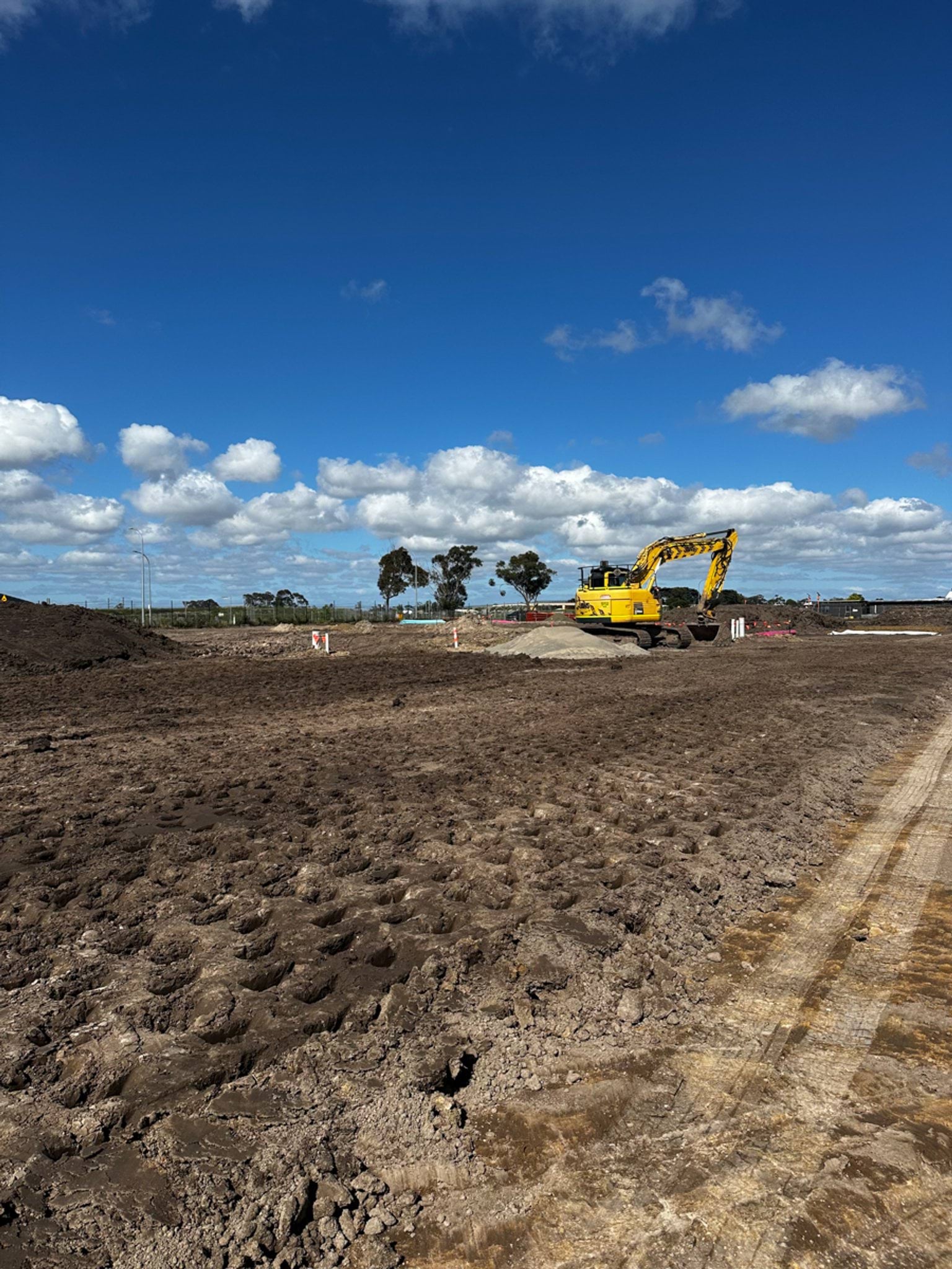 A construction area with compacted earth and a yellow excavator working under a clear blue sky.