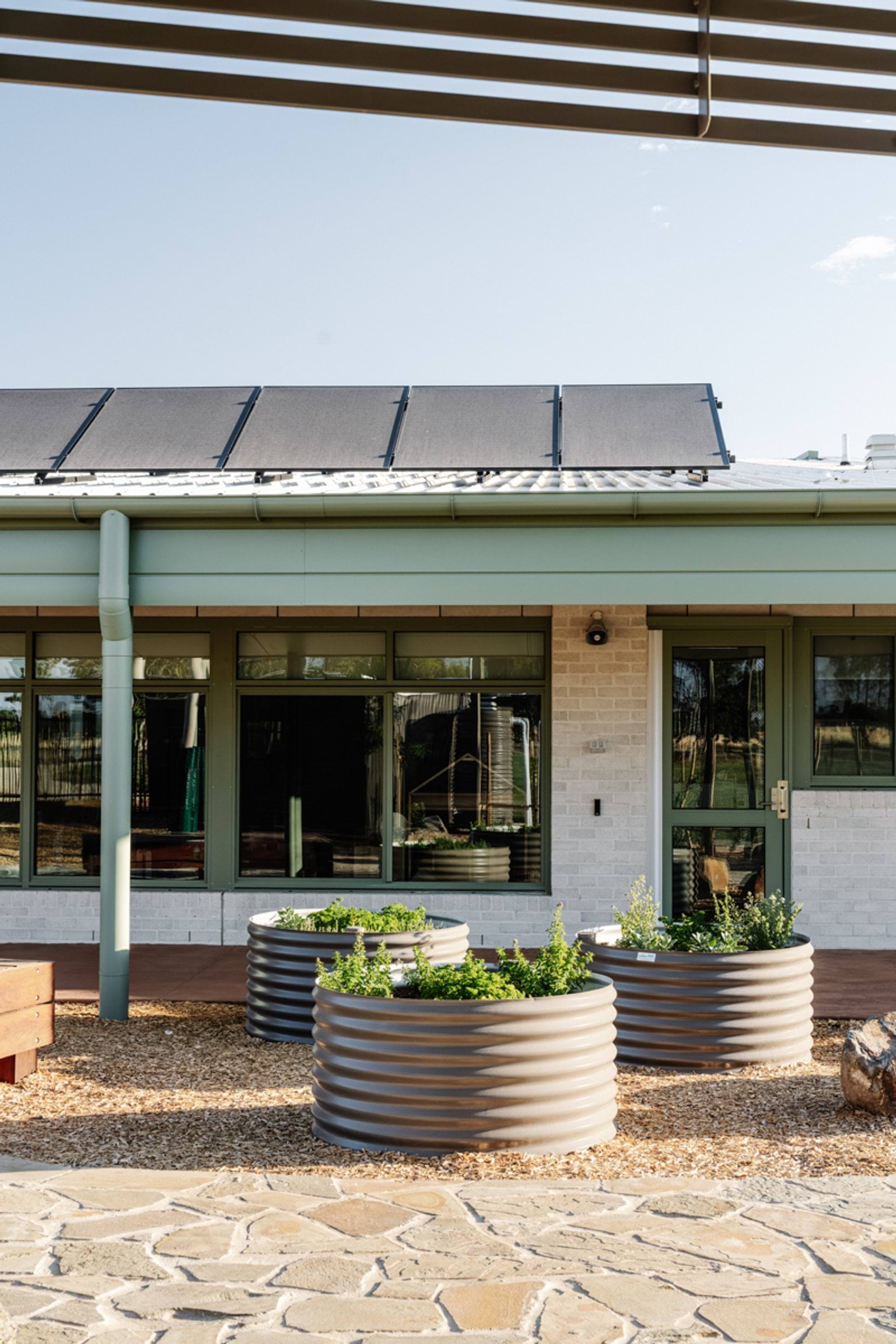 The exterior of a school building with raised metal garden beds and a row of windows beneath solar panels.