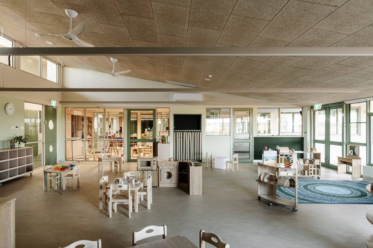 An indoor learning space with open shelving, tables and chairs, and views outside.