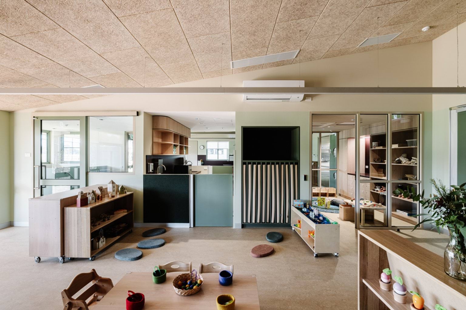 A large early learning classroom with small tables, timber play furniture, and activity zones arranged around the room.