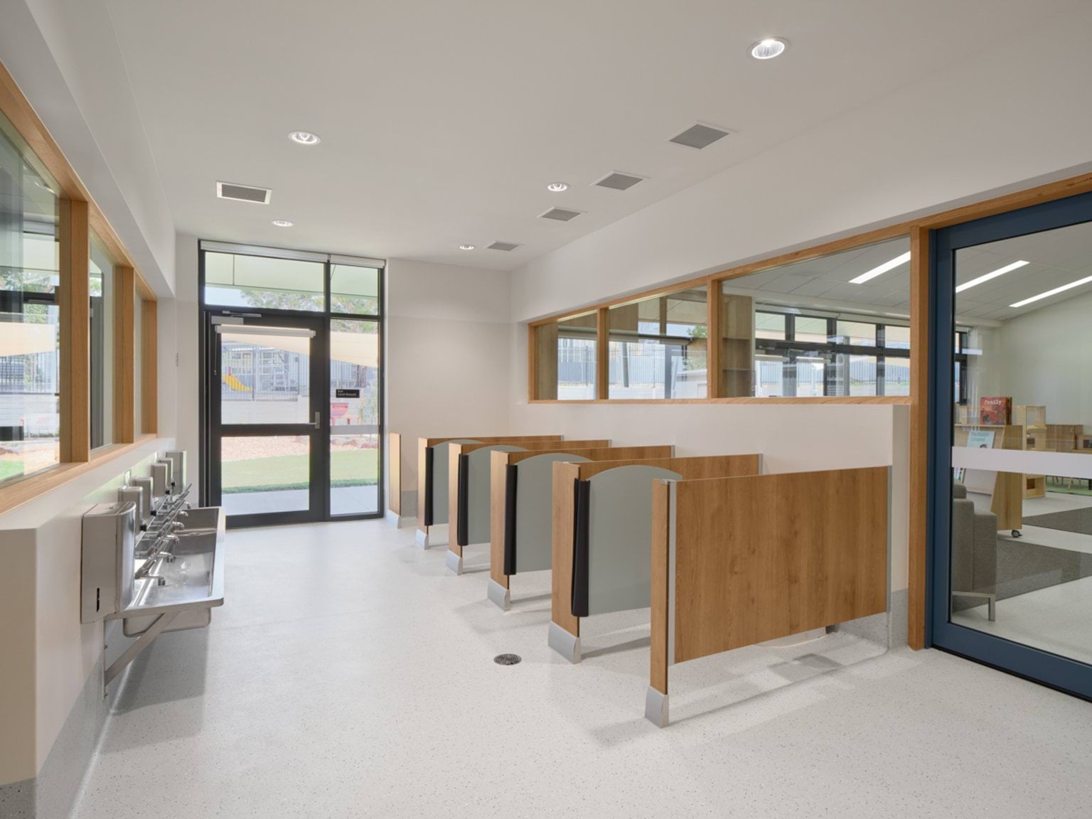 A children’s bathroom space with individual cubicles, handwashing sinks, and large windows overlooking the outdoor area.