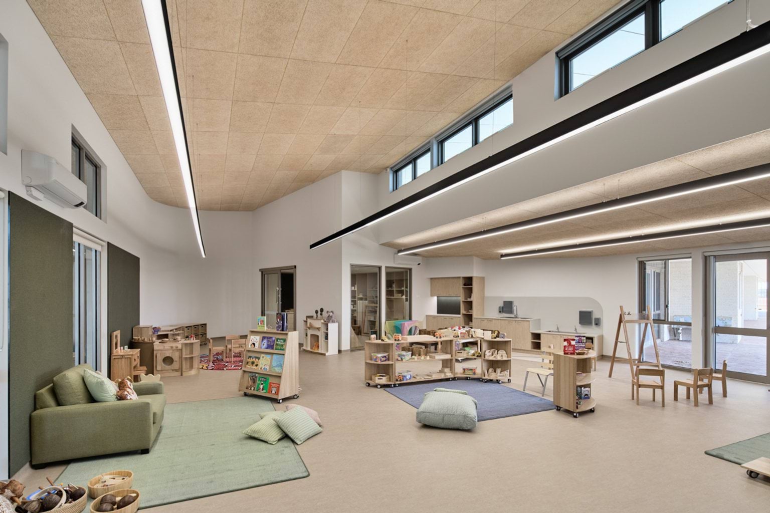 A light-filled reading room with seating, bookshelves, craft tables, and cushions.