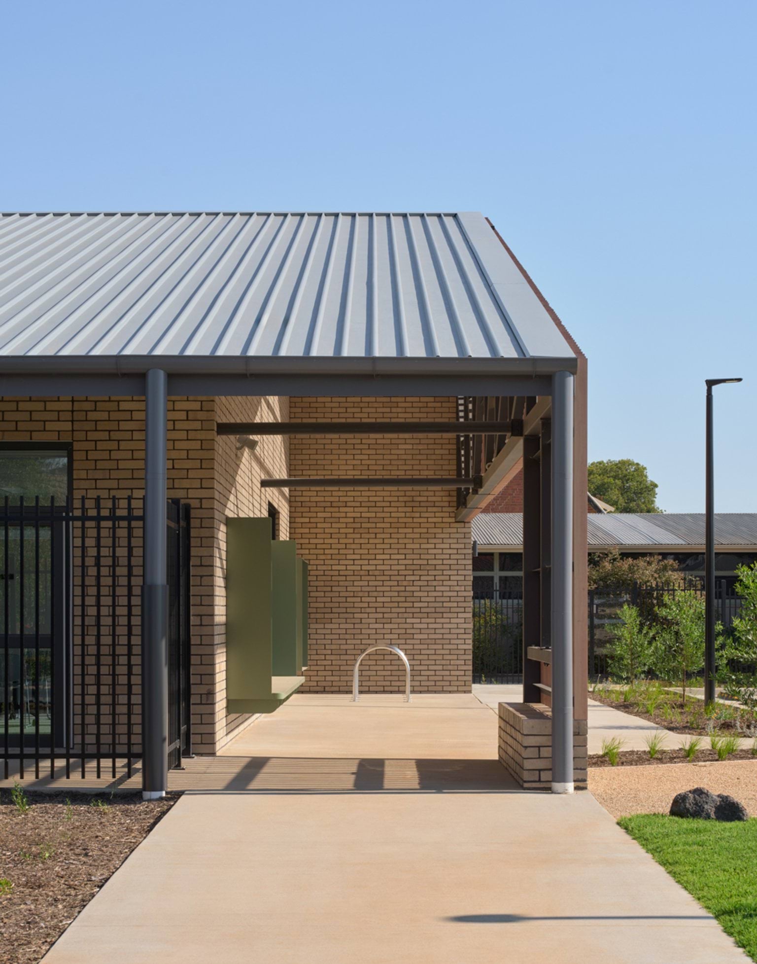 A covered walkway along the building’s side, featuring brick walls, a metal roof, and landscaped garden beds.