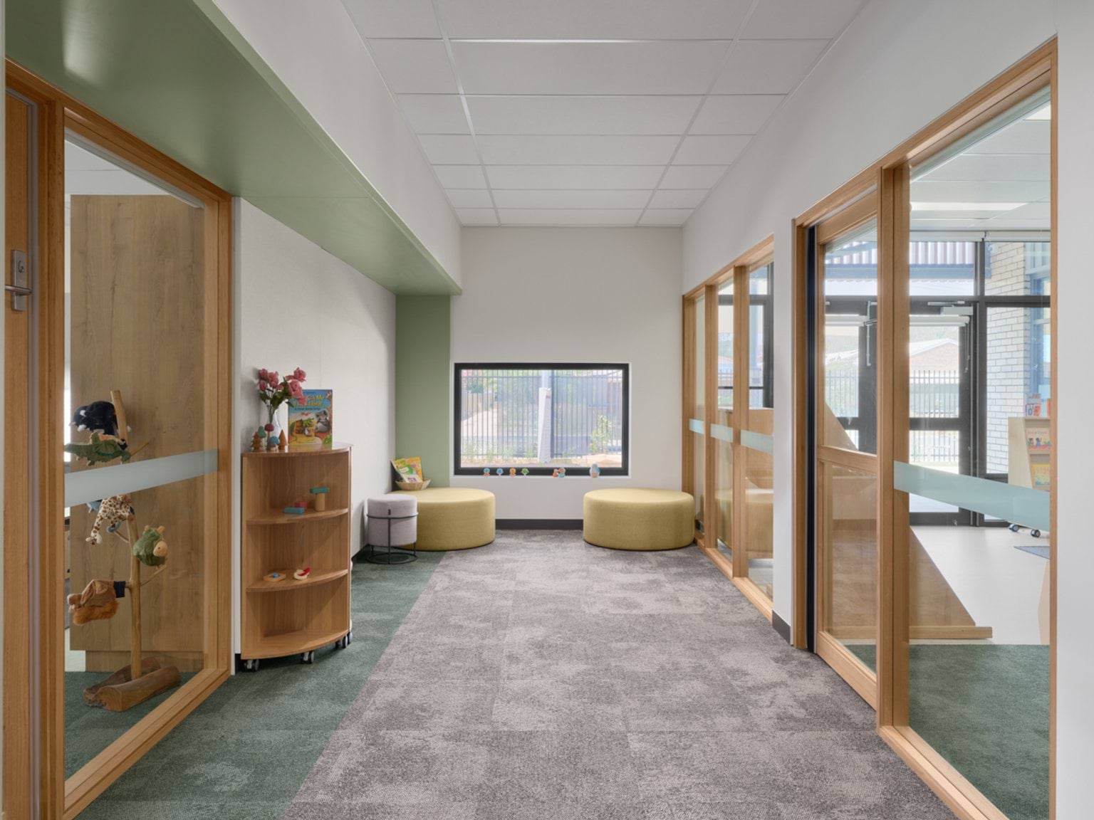 A breakout area with a low window, round cushioned stools, and glass doors to adjoining learning rooms.