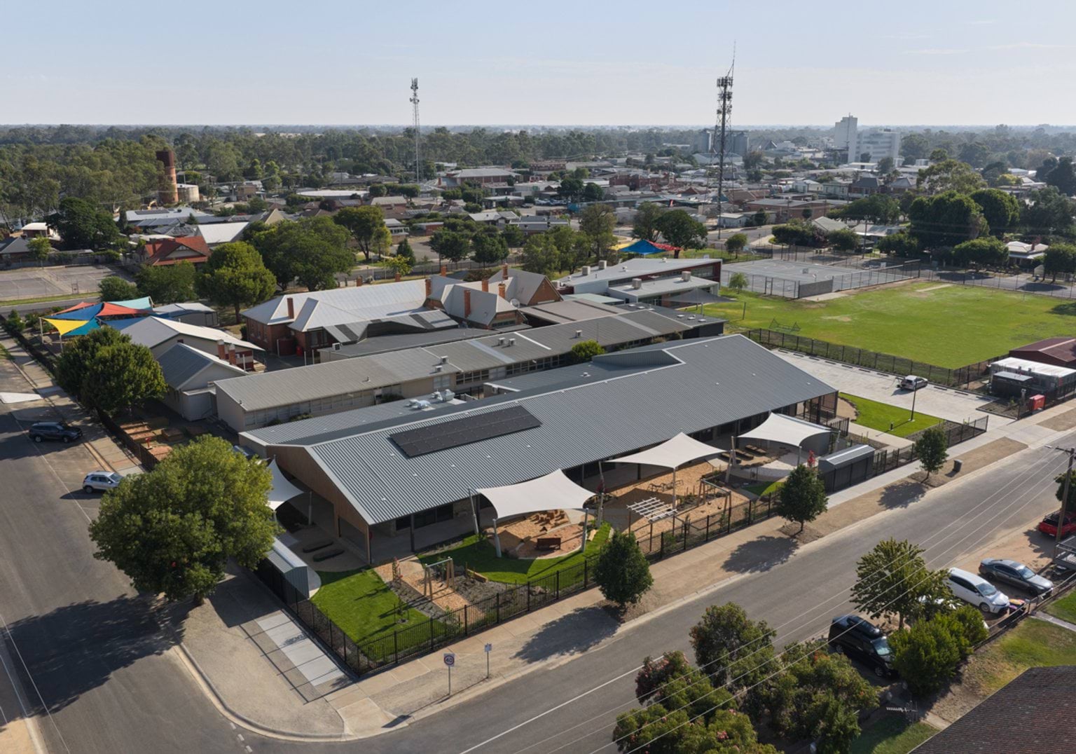 Aerial view of the centre within the wider neighbourhood, with outdoor play areas, car parking, and nearby sports fields.
