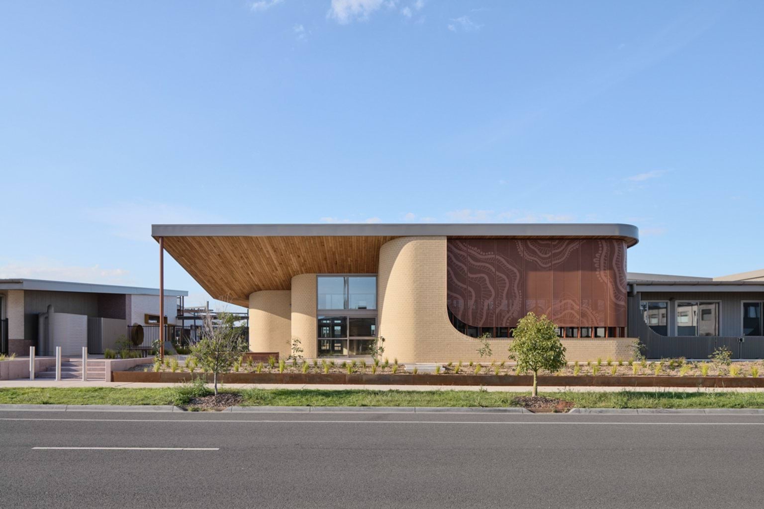 A street‑front view of the early learning centre with a curved roof, patterned screen panel, and landscaped planting along the footpath.