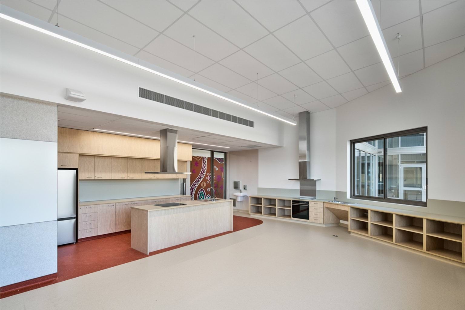 A light‑filled teaching kitchen with extensive bench space, storage cabinetry, two oven units, and a central island.