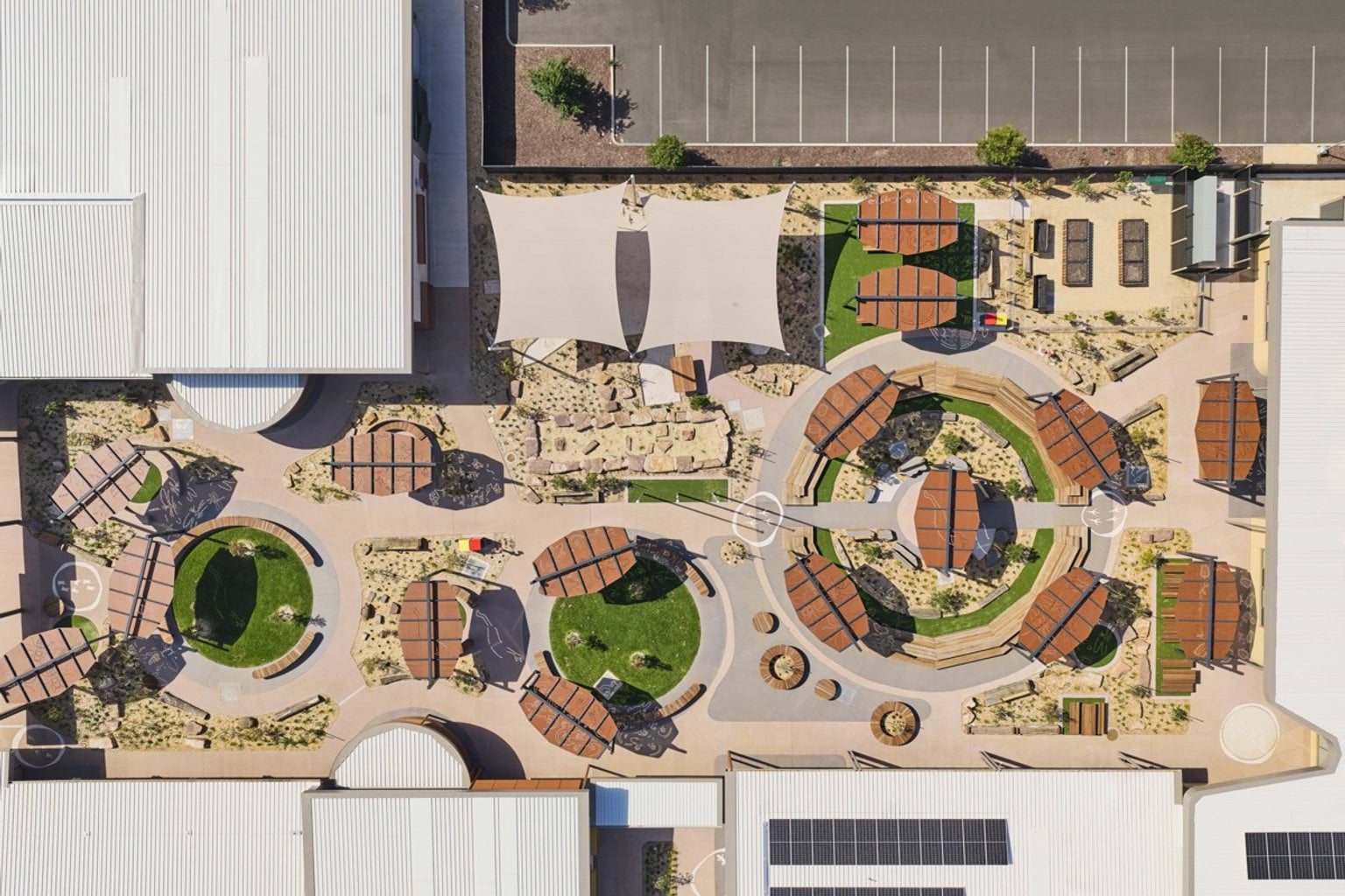 A top‑down view of a landscaped early learning outdoor play area with circular garden zones, timber shelters, and sand and climbing spaces.