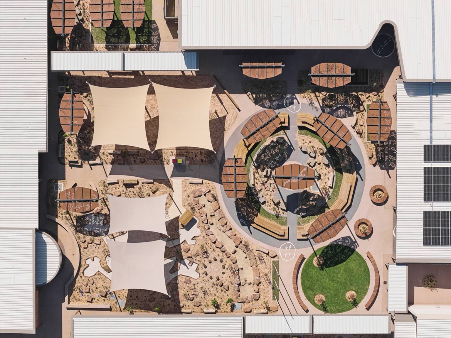 An outdoor courtyard with timber benches, plantings, and multiple patterned shade structures.