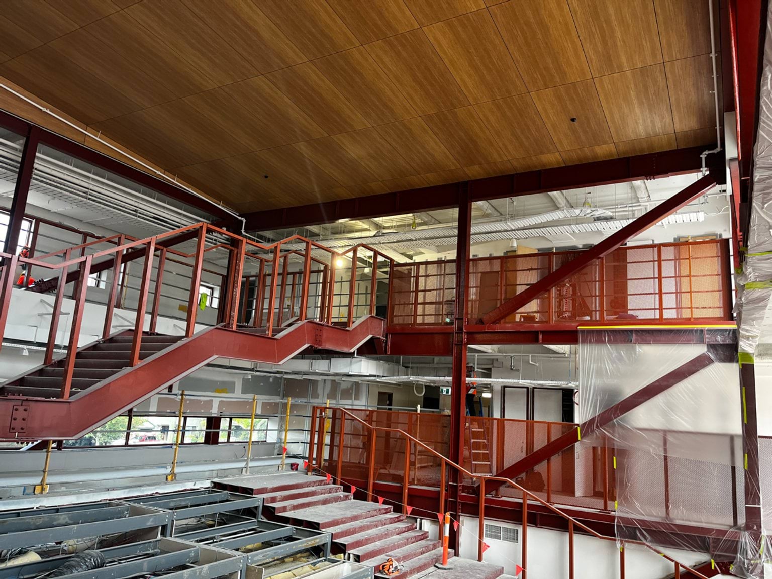 An interior atrium under construction featuring red steel staircases, timber ceiling panels, and exposed services.