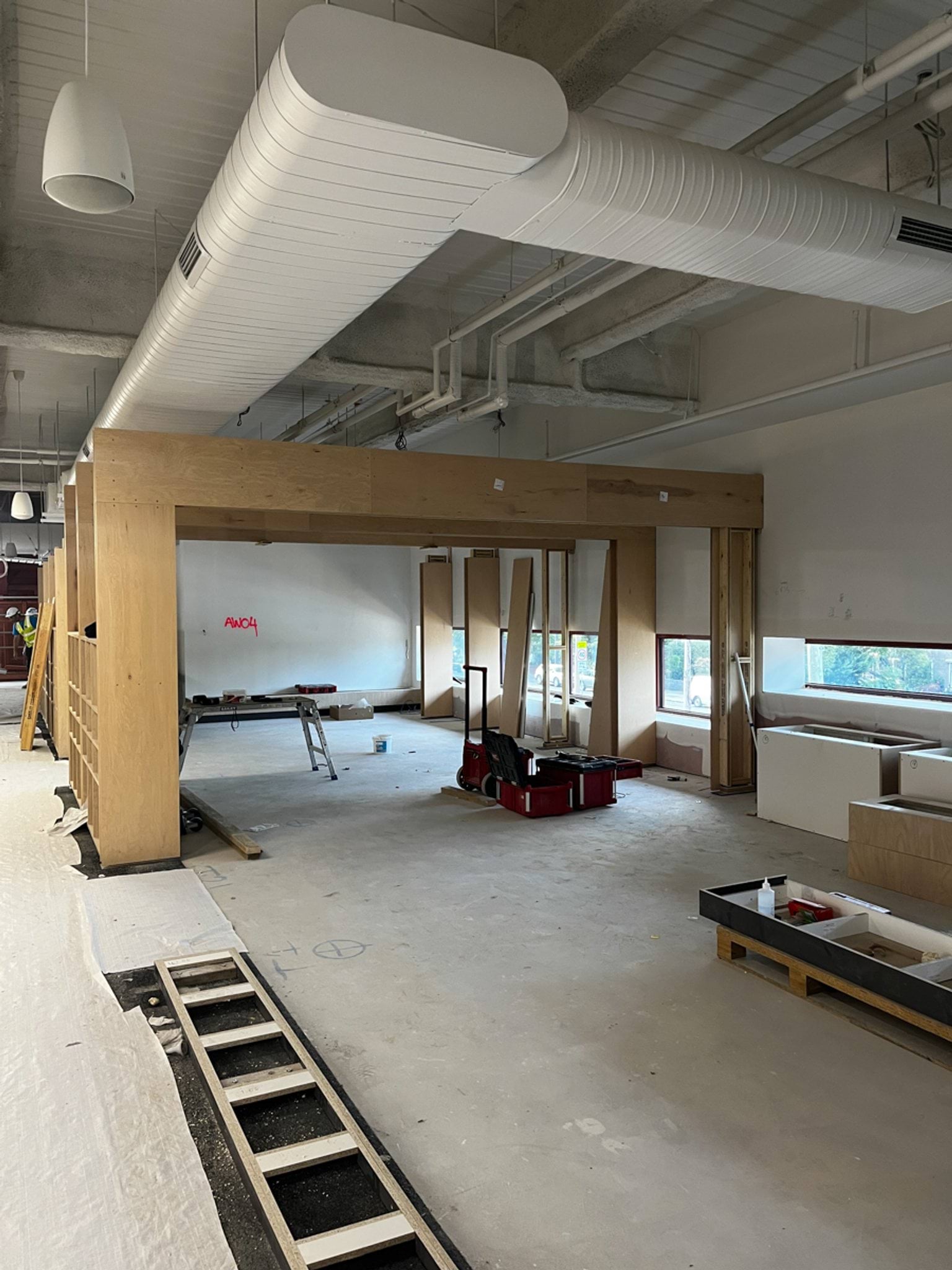 A school corridor under construction with shelving units, exposed ceiling services, and protective floor coverings.