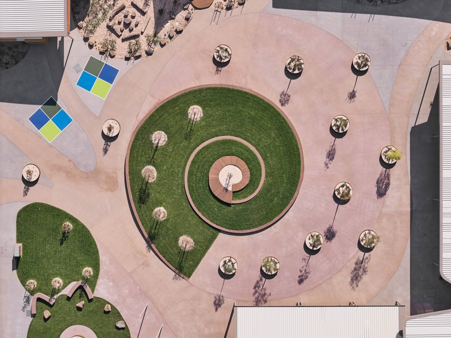 A top‑down view of a landscaped circular courtyard with a spiral grass design, surrounding paths, and evenly spaced young trees.