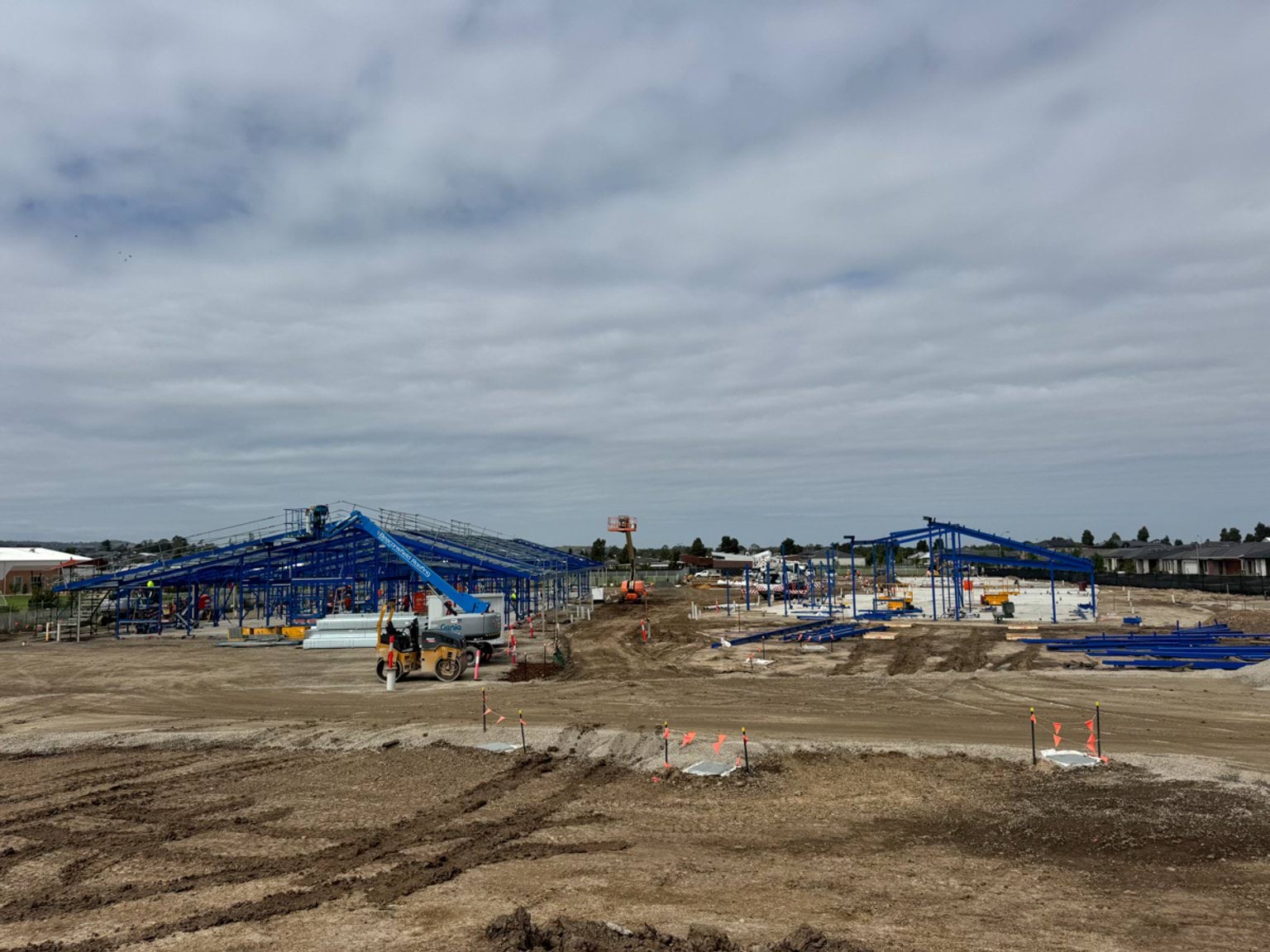 A wide view of the school construction site showing multiple steel-framed buildings being assembled across the cleared land.