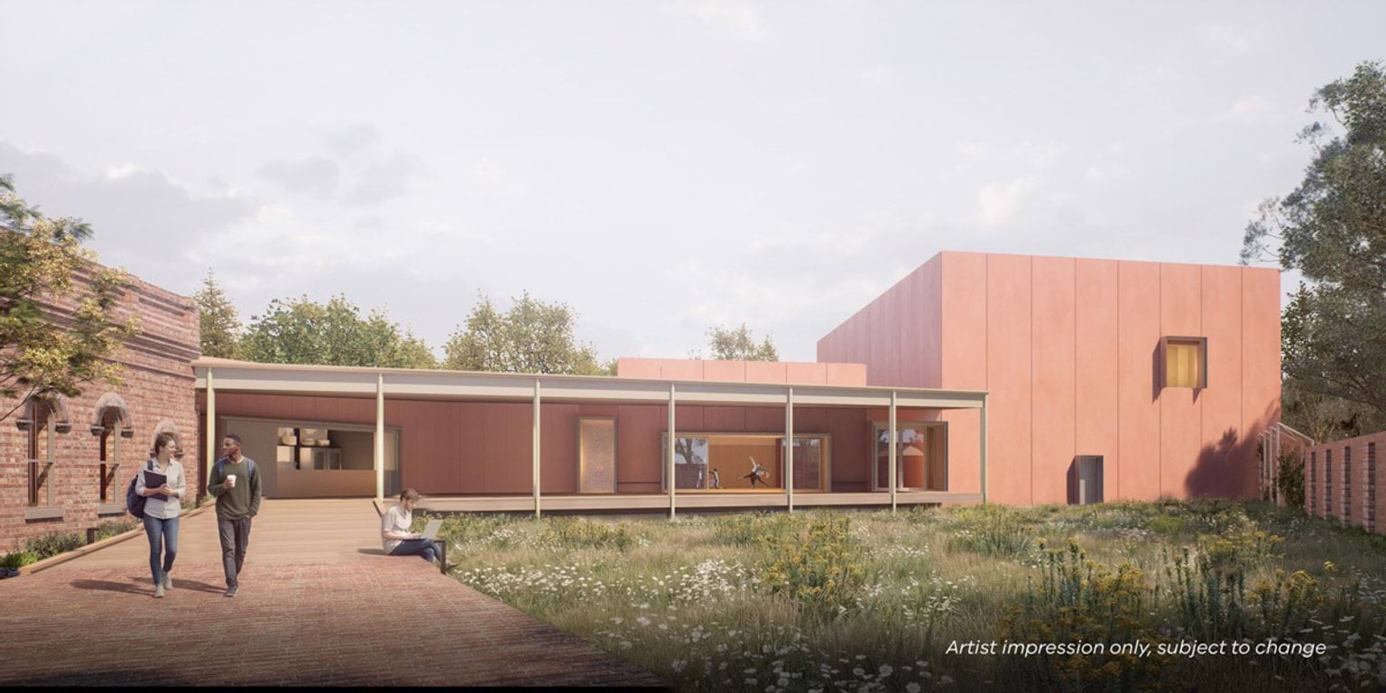 Path leading towards a red building with shaded walkway. There's grass and trees nearby.