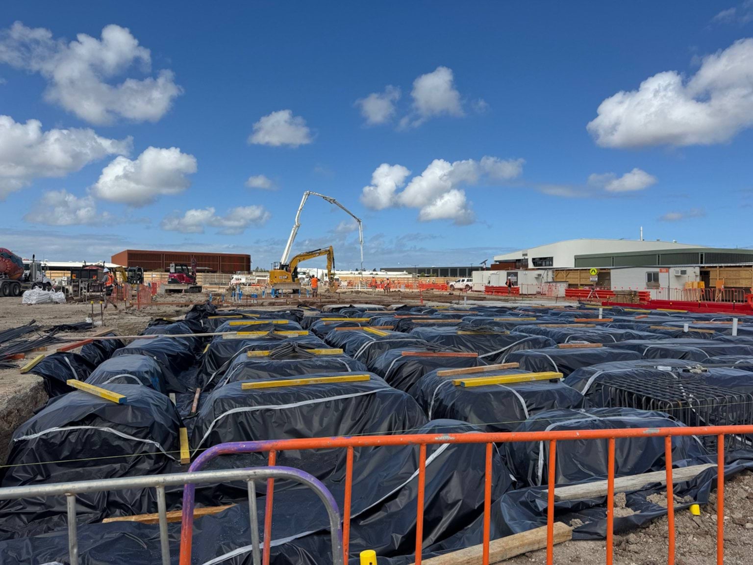Rows of wrapped foundation pods across the construction site, with cranes and machinery operating in the background on a clear day.