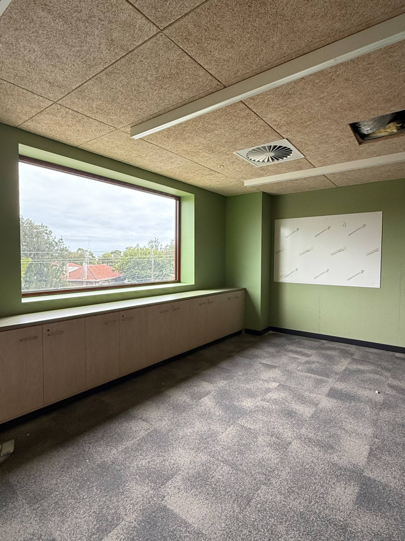 A bright classroom with green feature walls, built‑in cabinetry, and a large window overlooking nearby houses and trees.