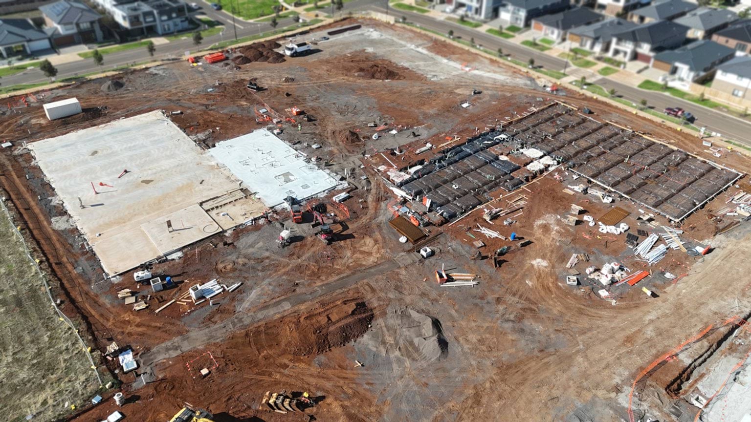Aerial view showing adjoining school building slabs at different construction stages, with workers and equipment visible across the site.