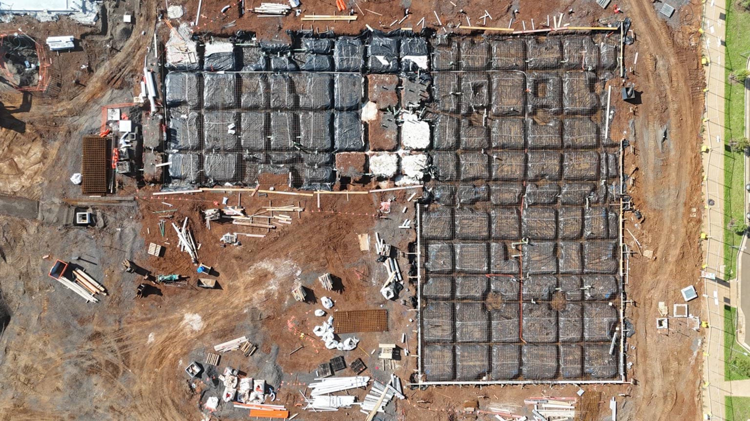 Close aerial view of a large foundation grid with steel reinforcement prepared for a concrete pour at the school site.