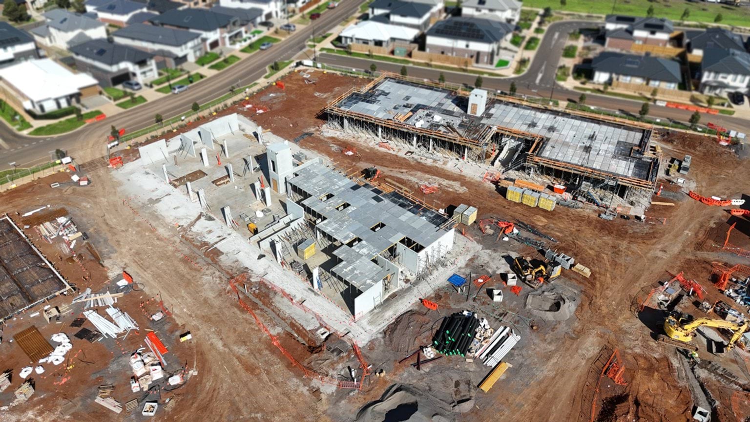 Aerial perspective of partially constructed school buildings with structural walls rising from concrete slabs.