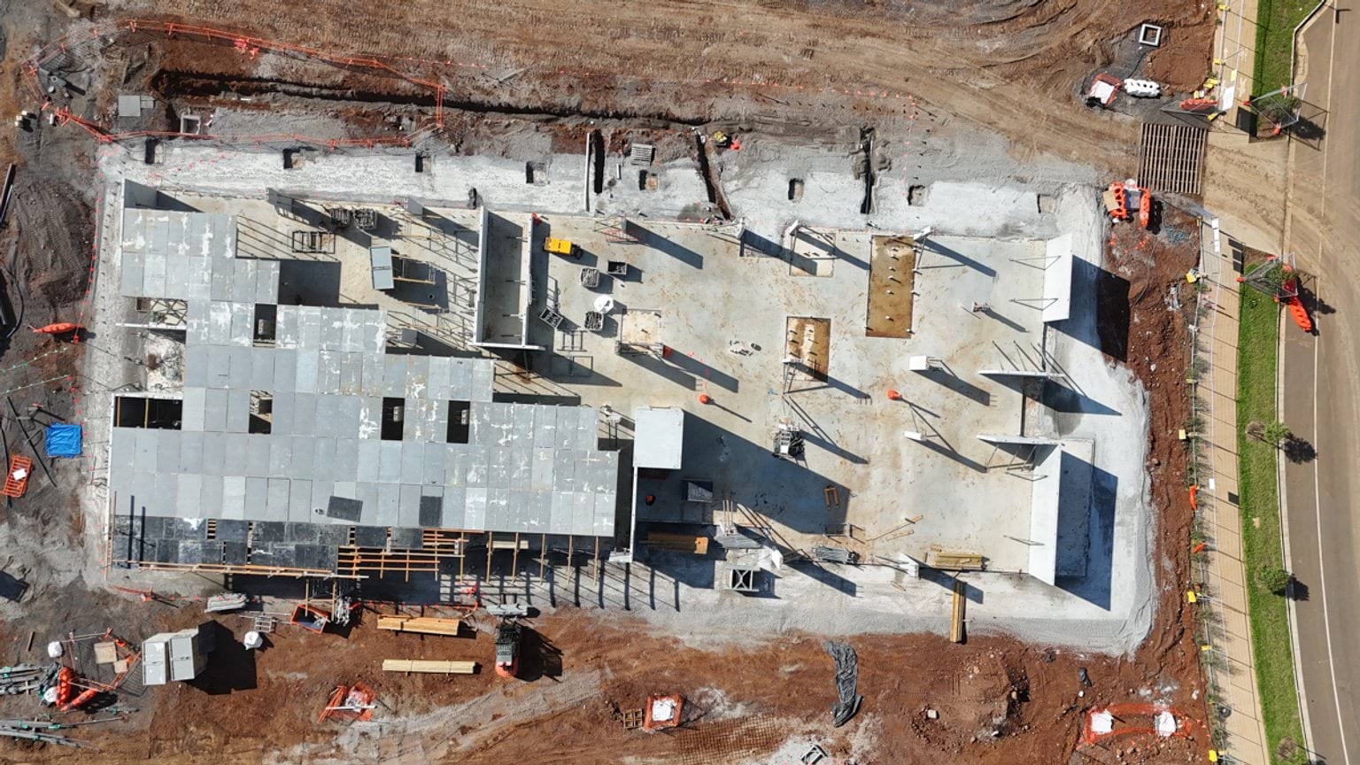 Aerial view of a school building slab under construction, showing concrete roofing sections, formwork, and materials laid out on site.