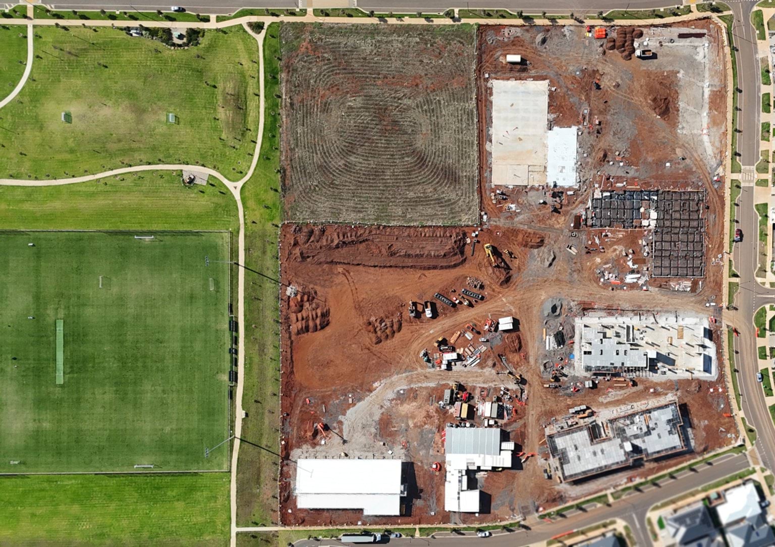 Wide aerial view of a school construction site beside sports fields, with multiple building footprints and earthworks underway.