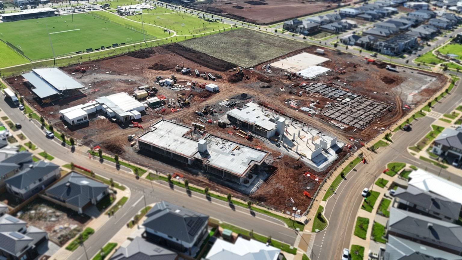Aerial view of the school site with several completed slabs, active building zones, and nearby housing estates.