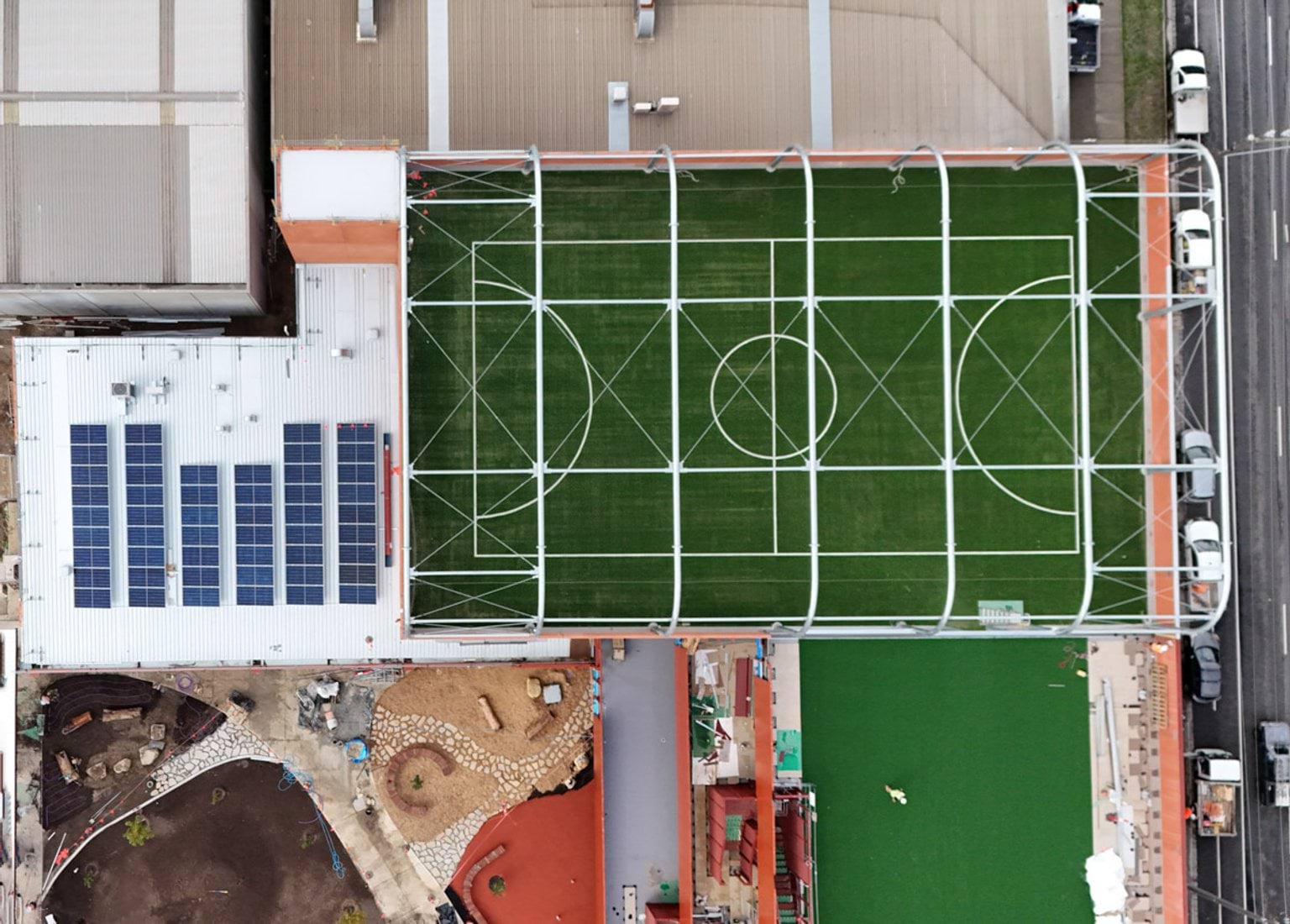 Top‑down aerial view of a rooftop sports court with marked basketball and netball lines beside solar panels.