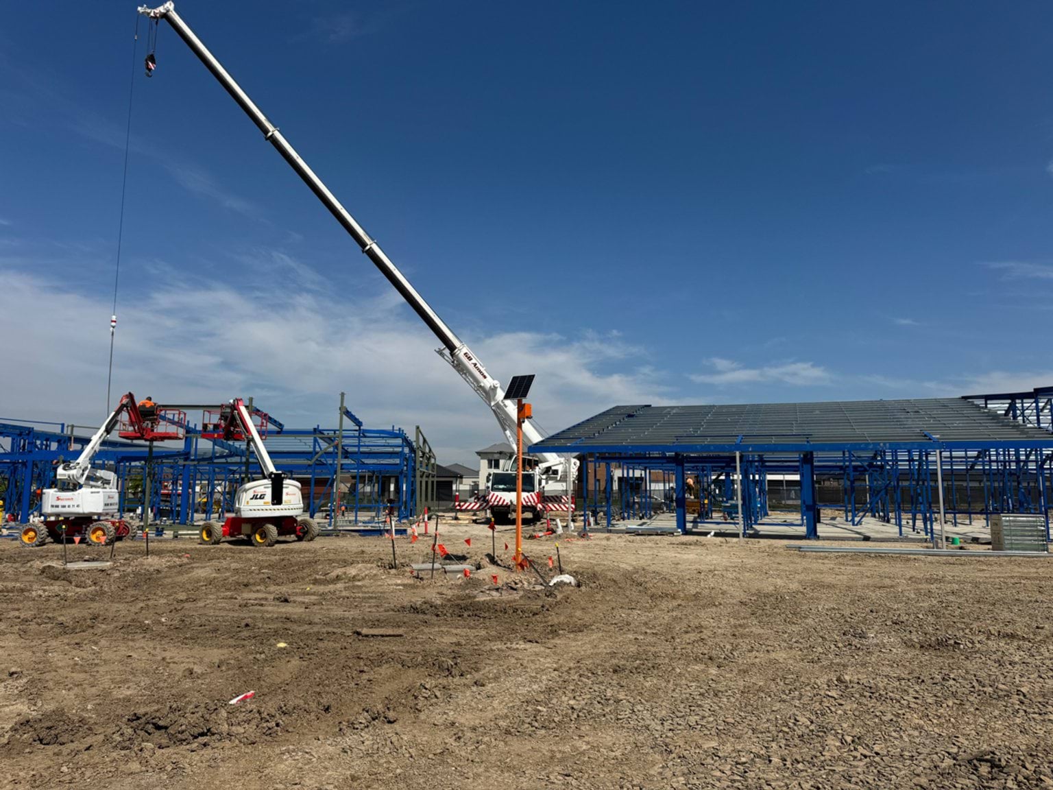 A wide school construction site with steel framing underway, including a crane and elevated work platforms operating on compacted soil.